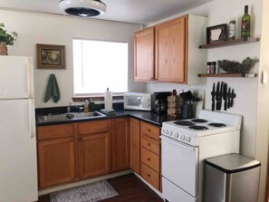 A compact kitchen with wooden cabinets, a white stove, a microwave, and a sink.