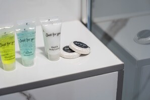 A white shelf with various toiletries including a hand and body lotion, a shower gel, and a shampoo conditioner. - Sutherland Apartments - Apt 24 (London)