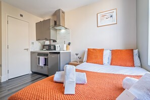 A hotel room with a bed, a kitchen area, and a framed picture on the wall. - Sutherland Apartments - Apt 24 (London)