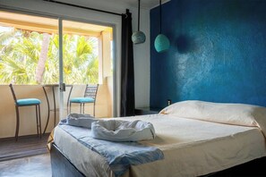 A bedroom with a bed, a window with a view of palm trees, a chair, and a blue wall. - Oceanview Hotel w/ Balcony, Steps to Zicatela (Puerto Escondido)