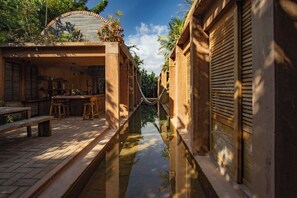 A narrow waterway between buildings with a wooden bench and stools, a small table, and a clear sky. - Oaxaca Villa: Private Pool, Beach Access & Garden (Puerto Escondido)