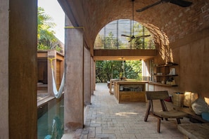 An indoor swimming pool area with a wooden bench, a hanging hammock, and a kitchen area with wooden shelves. - Oaxaca Villa: Private Pool, Beach Access & Garden (Puerto Escondido)