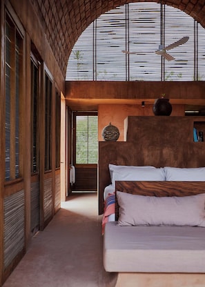Ein Schlafzimmer mit einem großen Bett, einem Deckenventilator und Blick durch ein Fenster mit Jalousien.