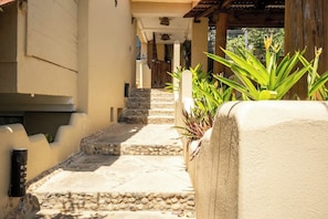 A narrow stone pathway leading to a building entrance, flanked by potted plants and a stone wall. - Oceanfront Apartment w/ Surf Views & Pool Access (Puerto Escondido)