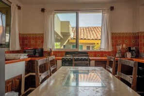 A kitchen with a dining table, a stove, and a window with curtains. - Oceanfront Apartment w/ Surf Views & Pool Access (Puerto Escondido)