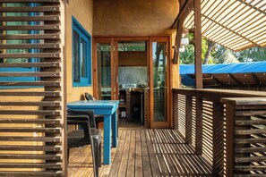 Eine Terrasse aus Holz mit Tisch und Stühlen, ein überdachter Bereich mit Grill und Blick auf die umliegende Landschaft.