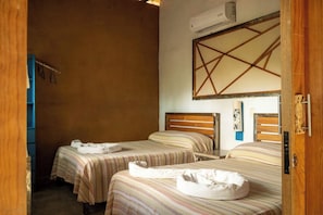 Ein Hotelzimmer mit zwei Betten, einem Holzkopfteil, einer Wandklimaanlage und einem blauen Schrank.
