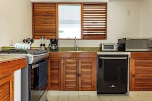 A compact kitchen with wooden cabinets, a built-in microwave, a coffee maker, and a dishwasher. - Beach Access Retreat w/ Garden Near 5th Ave (Playa del Carmen)