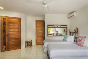 Ein Hotelzimmer mit zwei Betten, einem Deckenventilator, einer Klimaanlage und einer Holztür mit einer Klappkonstruktion.
