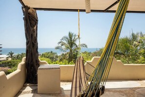 A hammock under a shaded area with a view of the ocean and palm trees. - Zicatela Oceanview Oasis: Pool, Hot Tub, Surf (Puerto Escondido)