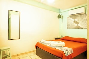 A room with a bed, a small stool, a wall-mounted air conditioner, and a mirror. - Zicatela Oceanview Oasis: Pool, Hot Tub, Surf (Puerto Escondido)