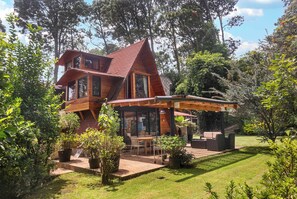 Una casa moderna de madera con techo inclinado, ventanas amplias y un patio con mobiliario exterior.