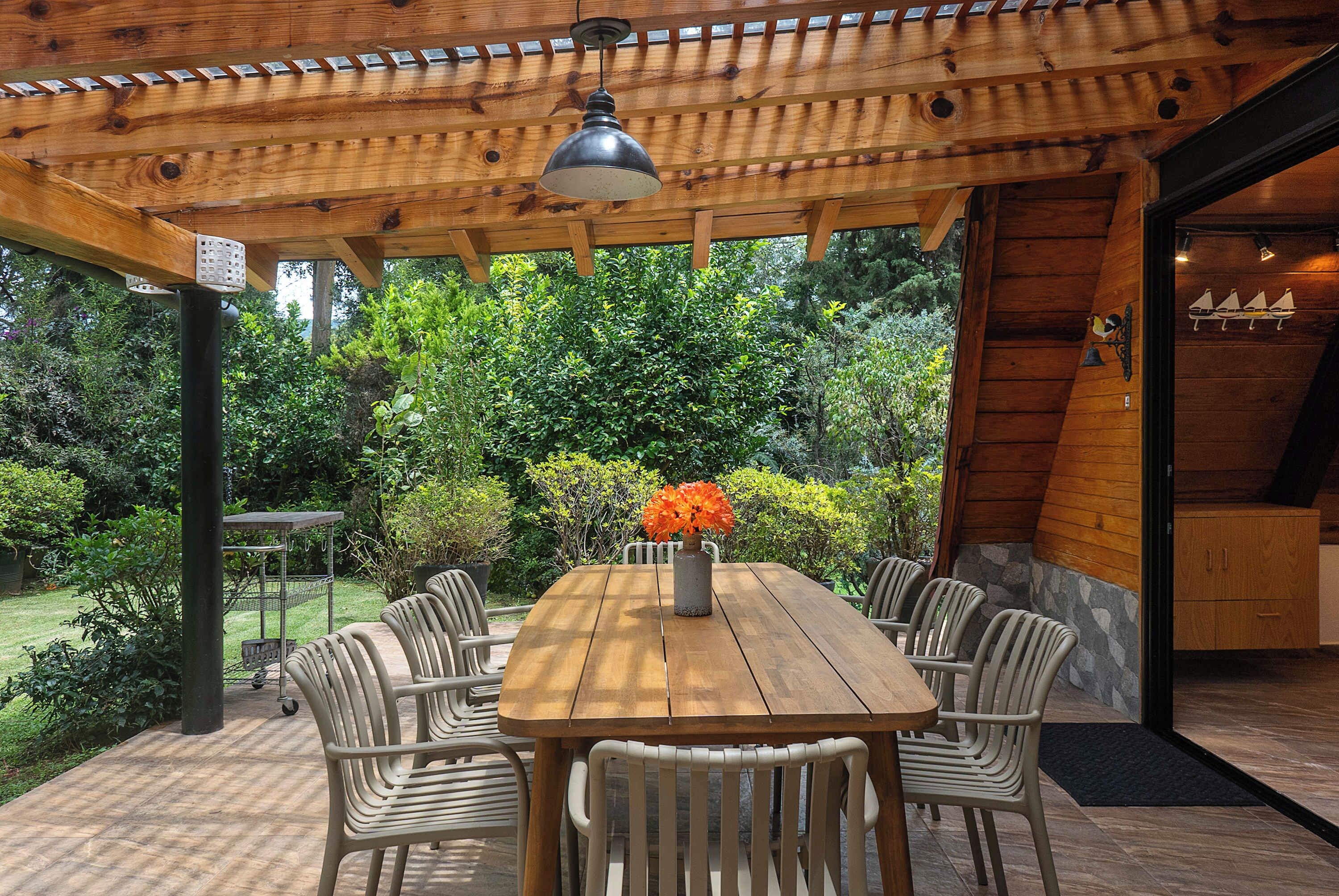 Une pergola en bois, avec une table et des chaises, entourée d’une végétation luxuriante.
