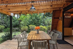 Una pérgola de madera con una mesa y sillas, rodeada de abundante follaje.