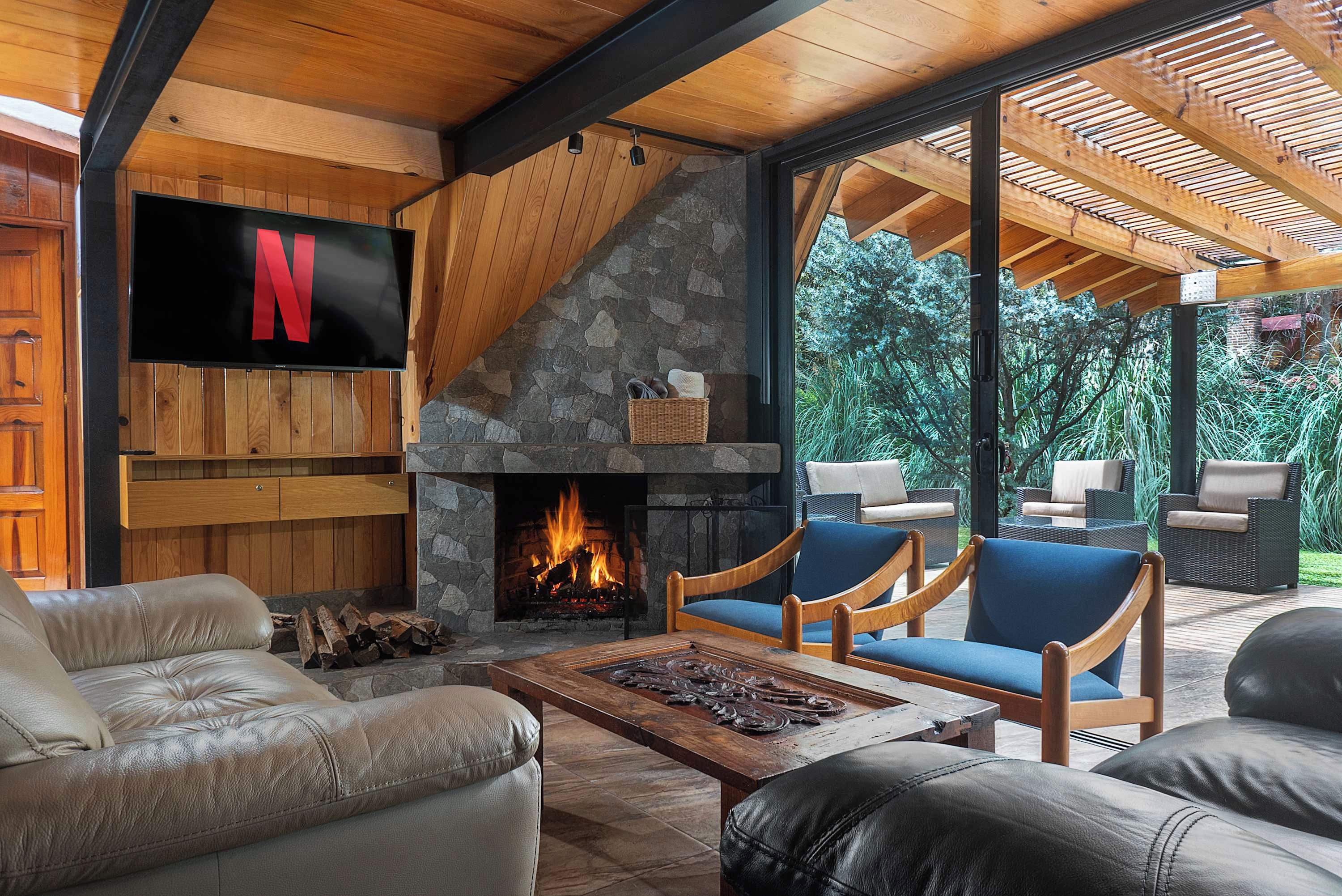 A cozy living room with a stone fireplace, comfortable seating, and a flat-screen TV mounted on the wall.
