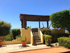 A staircase leading to a wooden pergola, surrounded by potted plants and a clear blue sky. - Oceanview Apt w/ Pool, Zicatela Surf Proximity (Puerto Escondido)