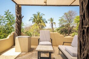 An outdoor seating area with a table and two chairs, surrounded by a beige wall and a view of palm trees. - Tropical Hotel w/ Pool, Steps to Zicatela Beach (Puerto escondido)