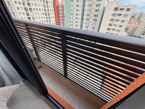 Un balcone con ringhiera in metallo, vista su edifici a più piani e pavimento piastrellato.