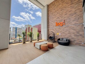 A modern lounge area with a view of the city skyline, a brick wall with a logo, and a hanging chair. - Comfort & Style in Downtown (Curitiba)