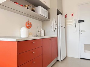 Una cucina con un piano di lavoro bianco, mobili rossi, un frigorifero bianco e un forno a microonde sullo scaffale.