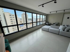 A spacious living room with a large window, a white sofa, and a green chair. - Comfort & Style in Downtown (Curitiba)