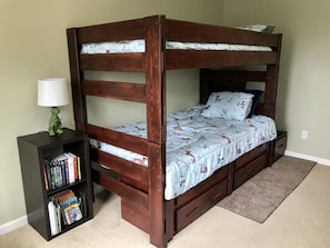 A bunk bed with a wooden frame, a bedside table with a lamp, and a bookshelf filled with books. - Centrally Located Eugene Home w/ Patio & Air (Eugene)