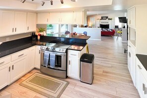 A modern kitchen with white cabinets, a stainless steel stove, and a black countertop. - Happy Heart House | Hot Tub | Firepit (Eugene)
