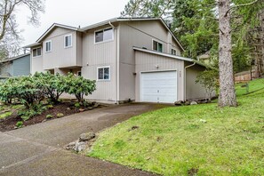 A two-story house with a garage, a driveway, and a small garden with shrubs. - Renovated Duplex Near Trails & UofO, Fenced Yard (Eugene)