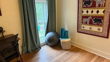 A room with a wooden floor, a desk with a chair, a large exercise ball, and a basket with yoga mats.