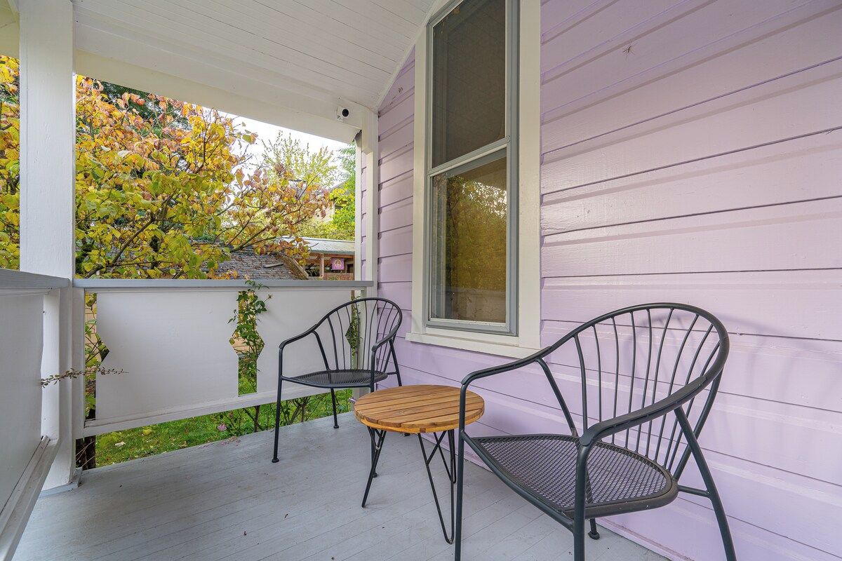 A porch with a wooden table and two chairs, a window, and a view of trees.