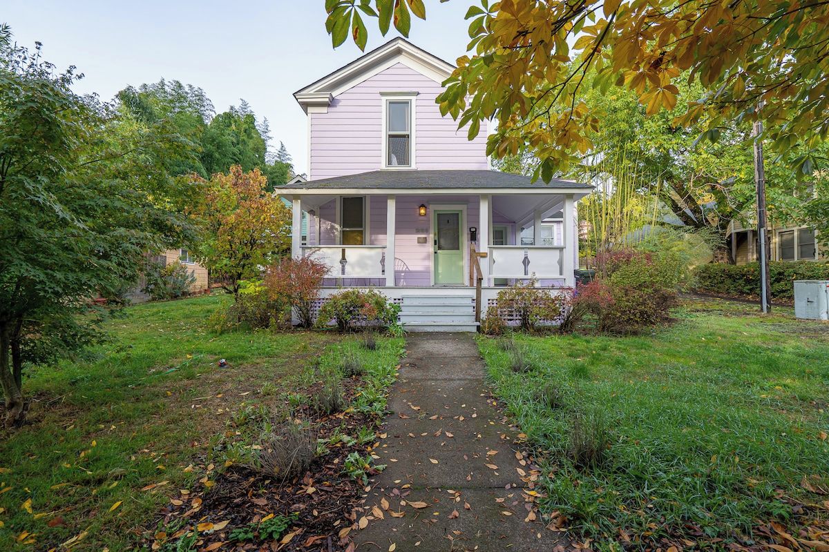 A single-story house with a front porch, a pathway leading to the entrance, and a garden with various plants and trees.