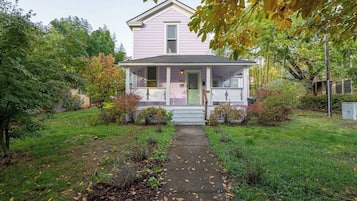 A single-story house with a front porch, a pathway leading to the entrance, and a garden with various plants and trees.