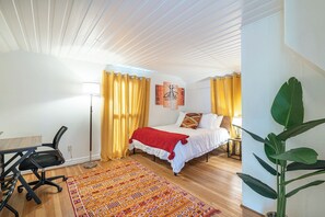 Ein Hotelzimmer mit einem Bett, einem Schreibtisch, einem Sessel, einer Stehlampe, einer großen Pflanze und einem gemusterten Teppich.