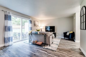 A living room with a sofa, TV, and a table with books and a lamp. - PNW Forest Getaway w/Fenced Yard & Central Air (Eugene)