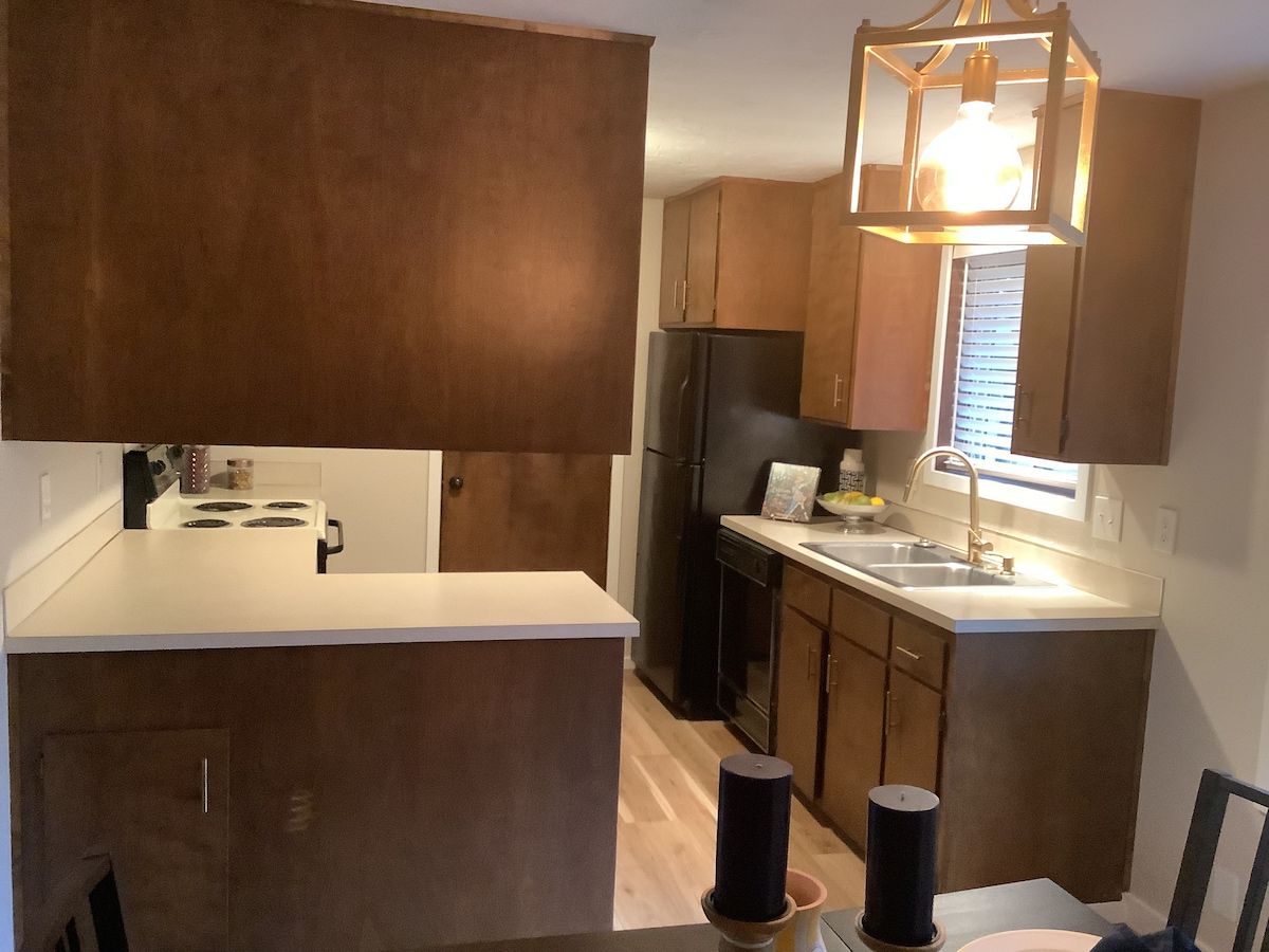 Une cuisine avec un plan de travail blanc, des meubles en bois foncé, un réfrigérateur noir et un luminaire suspendu.