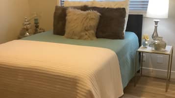 A bedroom with a bed, pillows, a nightstand, a lamp, and a window with blinds.