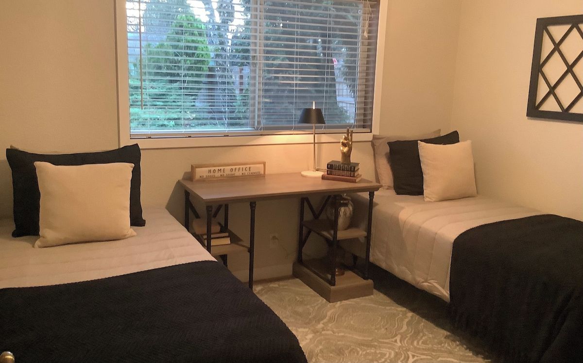 Une chambre avec deux lits, un bureau et une fenêtre avec des stores.