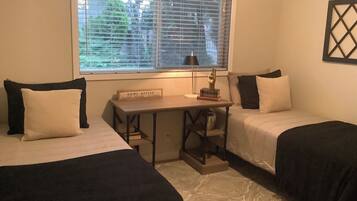 Une chambre avec deux lits, un bureau et une fenêtre avec des stores.