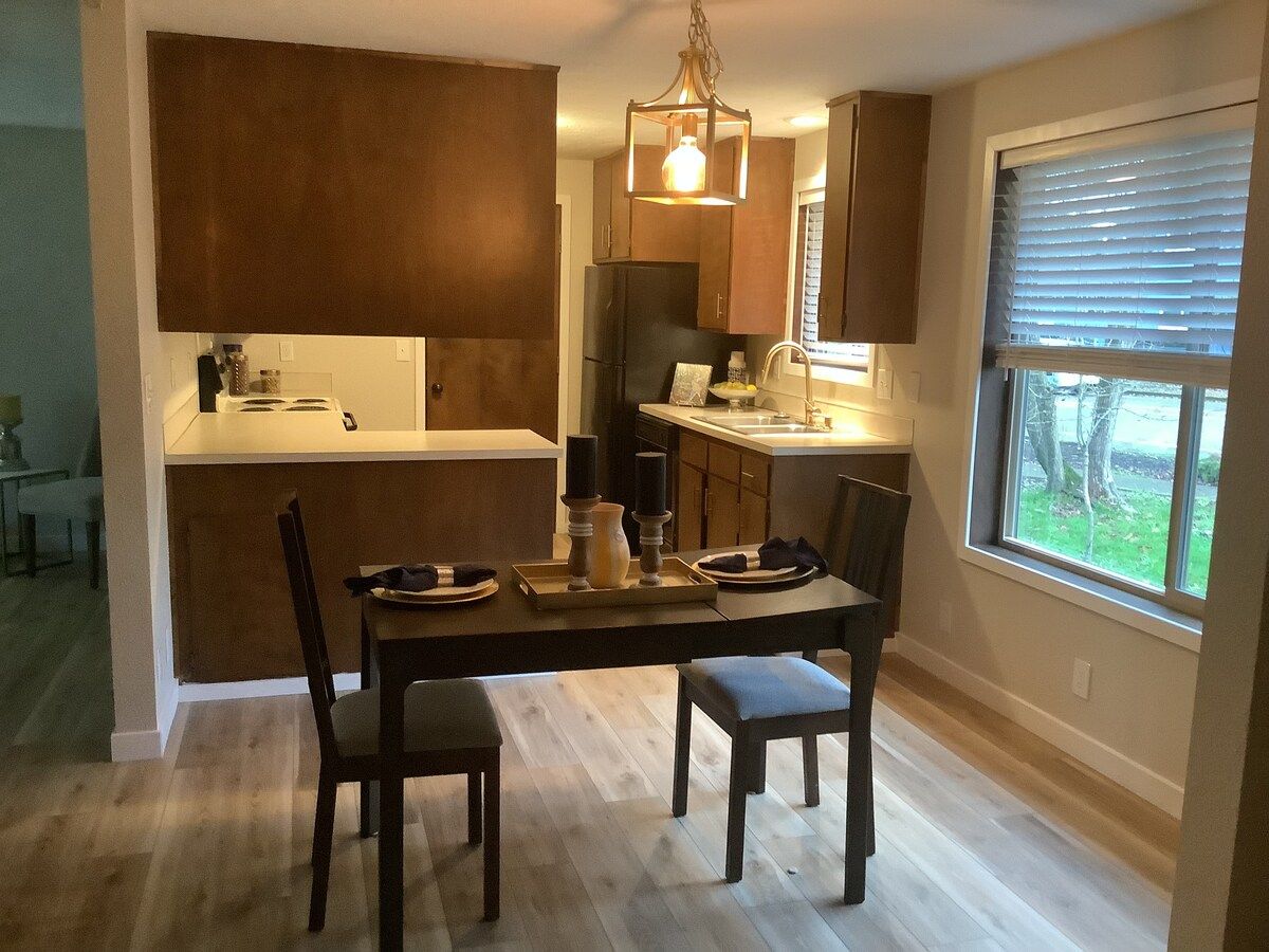 Une cuisine moderne avec des meubles de couleur sombre, un îlot central et un coin repas comprenant une table et des chaises.