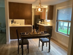 A modern kitchen with dark cabinetry, a central island, and a dining area with a table and chairs. - 2 Bedroom desirable Ferry Street Bridge ! Casa 15 (Eugene)