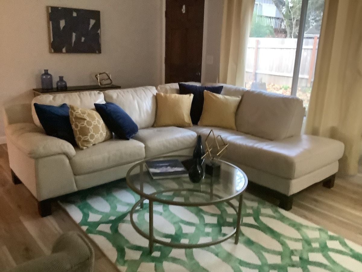 A living room with a sectional sofa, a glass coffee table, and a patterned rug.