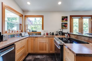 A kitchen with wooden cabinets, a built-in oven, a sink, and a window with a view of trees. - Amazon Area Backyard ADU With Private Entrance (Eugene)