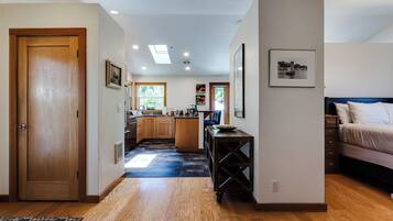 Un intérieur moderne avec un plancher en bois, une cuisine dotée de meubles en bois, un coin repas avec une table et des chaises, et une chambre à coucher avec un lit et une table de chevet.