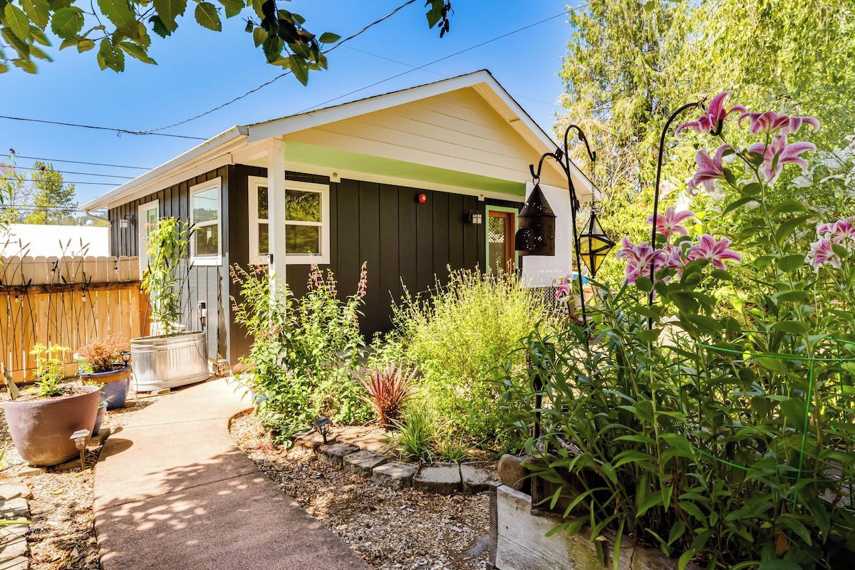 A small house with a porch, surrounded by various plants and a garden.