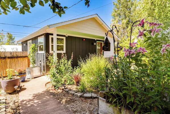 A small house with a porch, surrounded by various plants and a garden.