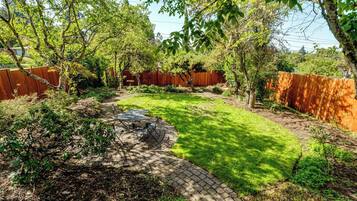 Un jardin avec une terrasse dallée, une pelouse et une clôture en bois.