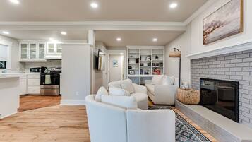 Un salon moderne avec une cheminée, des meubles blancs et une cuisine en arrière-plan.