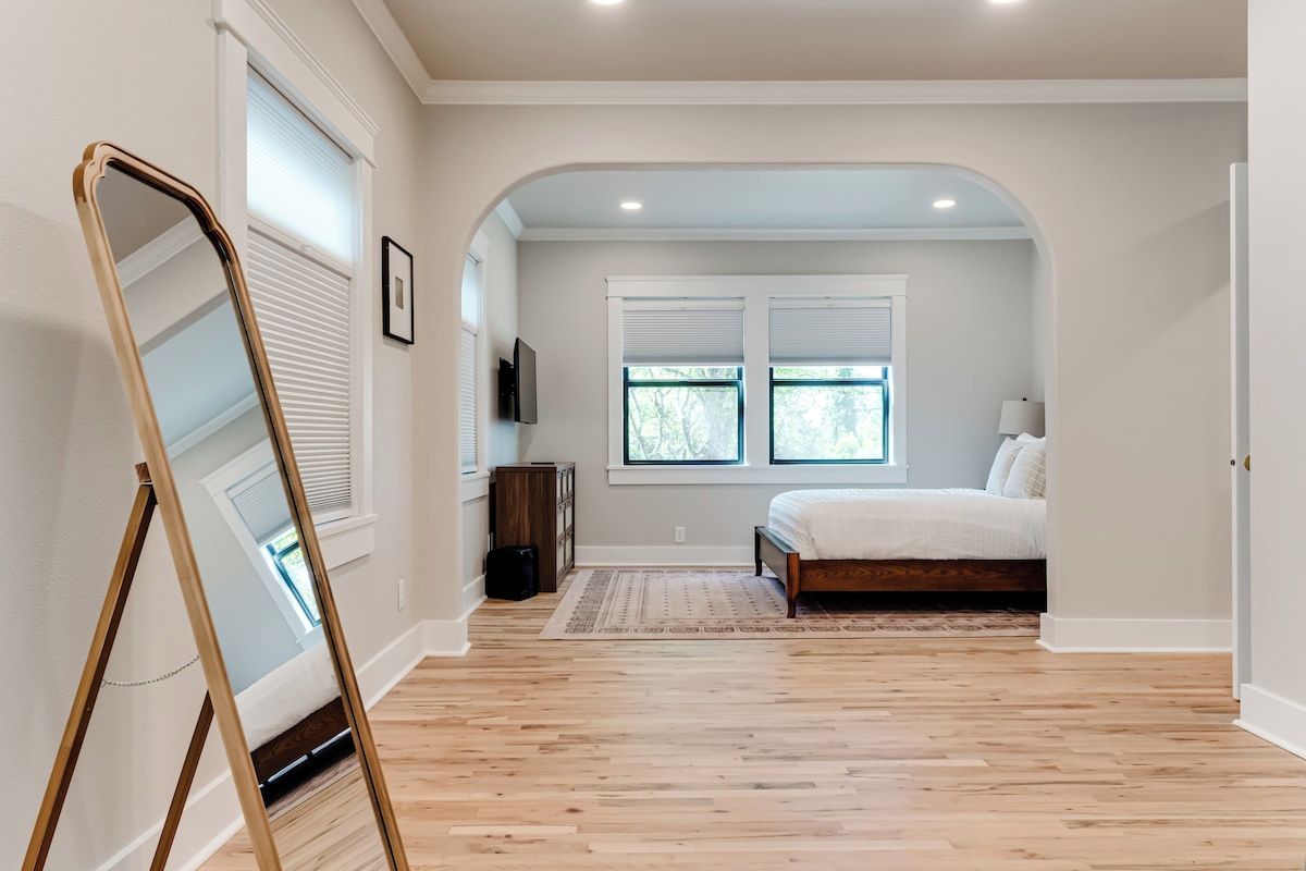 Une chambre à coucher avec un lit, un plancher en bois, une fenêtre et un téléviseur fixé au mur.