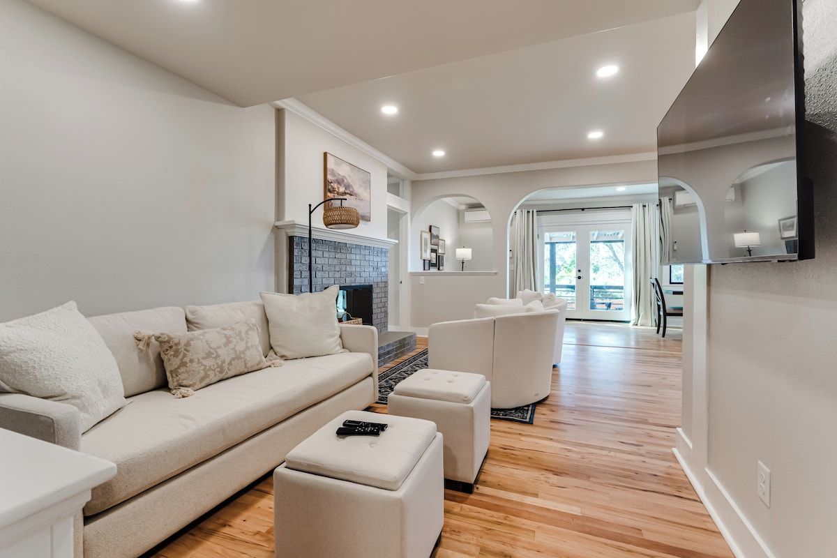 Un salon moderne avec un canapé, des poufs, une cheminée et, au fond, un coin repas.