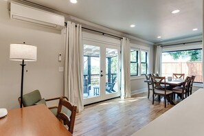A dining area with a wooden table and chairs, a lamp, and a view through glass doors to an outdoor patio.